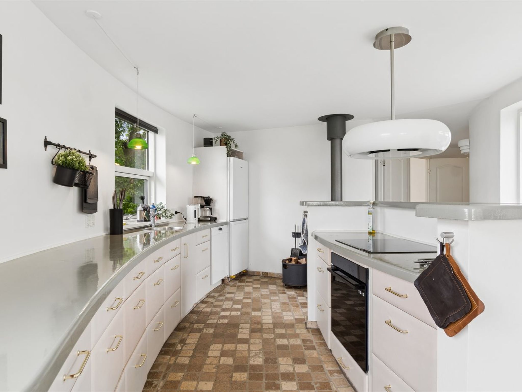 Eine moderne Küche mit weißen Schränken, einer gewölbten Arbeitsplatte, einem eingebauten Backofen und einer hängenden Pfannenleiste.