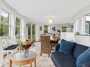 En moderne stue med en blå sofa, et rundt træbord med en vase blomster og en fletstol.