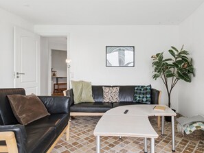 A living room with a black leather sofa, a white coffee table, and a plant.