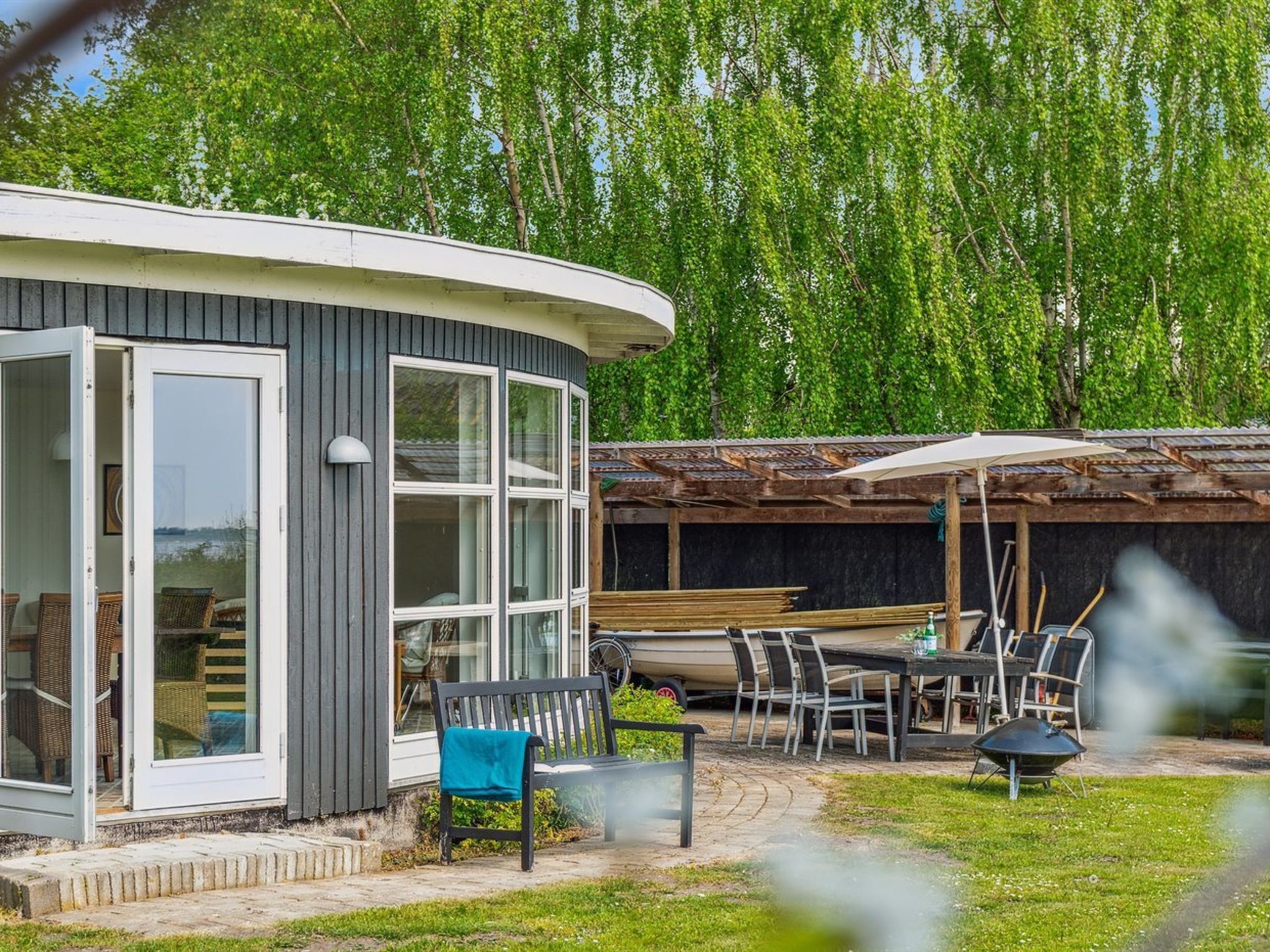 Une maison moderne à l’extérieur incurvé, dotée de grandes fenêtres et d’un patio aménagé avec du mobilier d’extérieur.