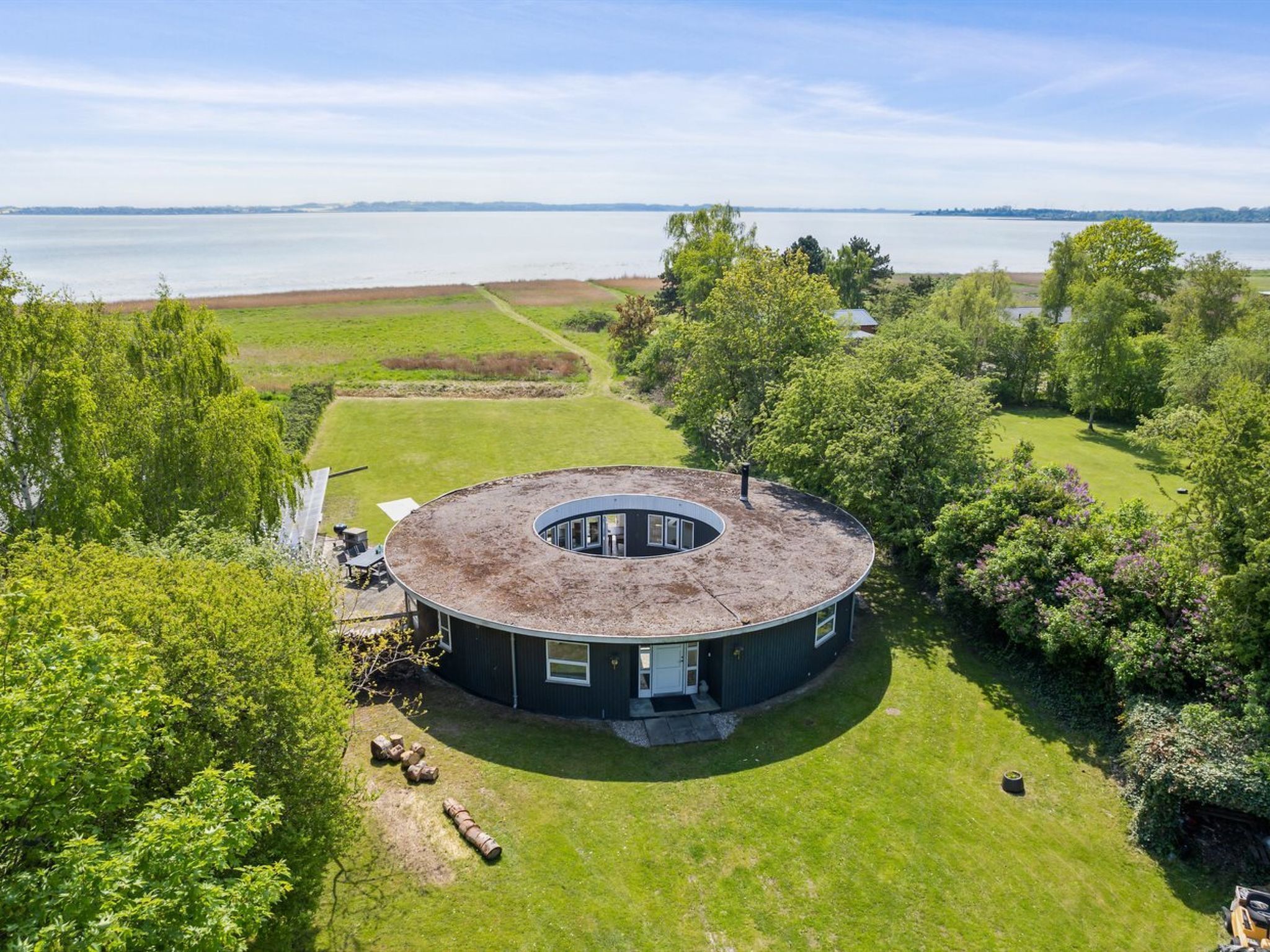 Un bâtiment circulaire doté d’un espace central ouvert, entouré d’une pelouse bien entretenue et d’arbres, avec une étendue d’eau en arrière-plan.