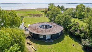 A circular building with a central open area, surrounded by a well-maintained lawn and trees, with a body of water in the background. - "Vemund" - 100m to the fjord by Interhome (Vig)