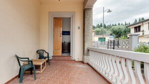 A balcony with a wooden table and chairs, a stone wall, and a view of neighboring buildings. - Apartment 'Ursa' with Shared Garden, Wi-Fi and Air Conditioning (Calenzano)