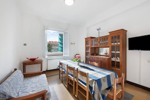 Un coin repas avec une table dressée pour quatre personnes, un meuble en bois, un téléviseur et une fenêtre donnant sur des immeubles.
