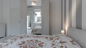 Quarto com cama, guarda-roupa, espelho e janela.