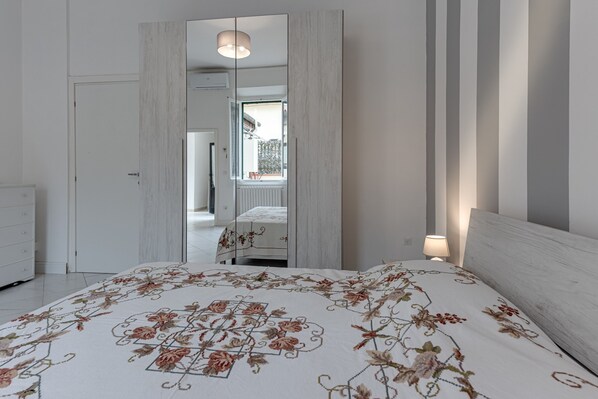 A bedroom with a bed, a wardrobe, a mirror, and a window.