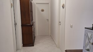 Um corredor com piso de azulejos brancos, um armário de madeira, uma porta com placa decorativa e um quadro pendurado na parede.