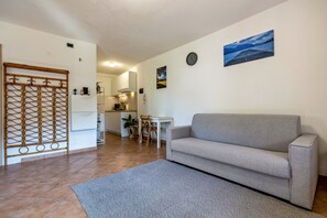 Een woonkamer met een grijze bank, een eettafel met stoelen, een keuken op de achtergrond, en een decoratieve roomdivider.