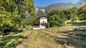 Une maison en pierre dotée d’un balcon, entourée d’arbres et de montagnes.