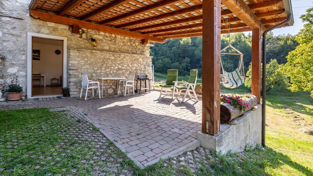 Un bâtiment en pierre agrémenté d’une pergola en bois, avec des sièges en plein air et une balançoire suspendue.