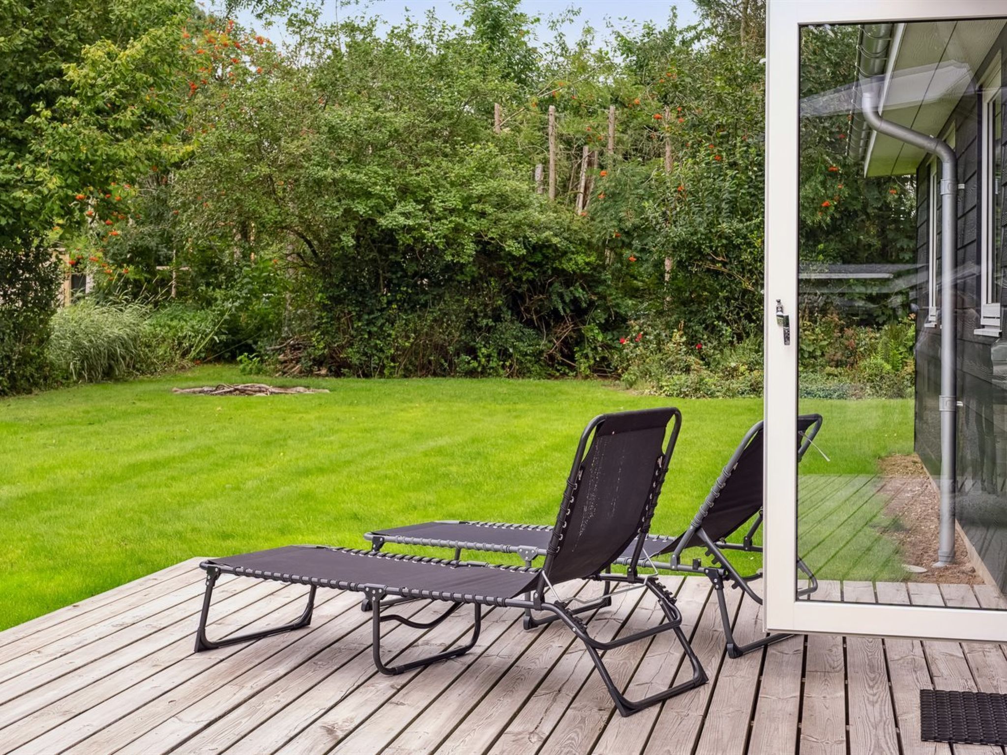 Una terrazza con due poltrone da relax e una porta vetrata che dà su un giardino con prato e vegetazione lussureggiante.