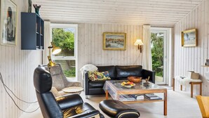 En hyggelig stue med en lædersofa, et sofabord med frugt og en reol.