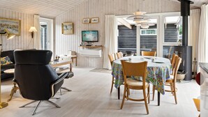 Et hyggeligt rum med et spisebord, stole, en sort læderstol, et fjernsyn og en pejs.