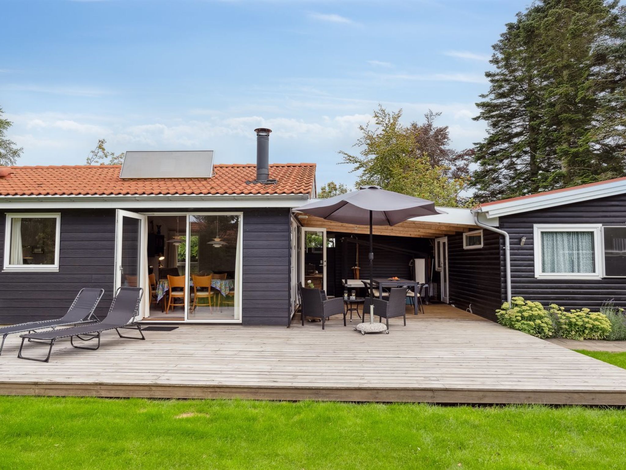 A modern house with a patio area featuring a table and chairs, a covered seating area, and a wooden deck.