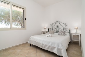 Une chambre à coucher avec un lit, deux tables de chevet, une fenêtre et une vue sur les arbres.
