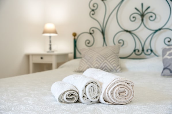 A neatly made bed with rolled white towels, a bedside lamp, and a decorative metal headboard.