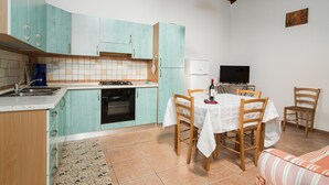 Une cuisine avec des armoires de couleur turquoise, une table à manger avec des chaises, un téléviseur et un réfrigérateur.