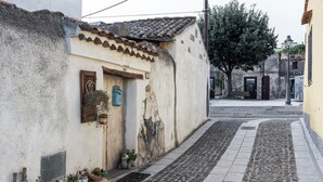 Une ruelle étroite pavée, bordée d’un immeuble orné d’une fresque murale, avec un banc et des plantes en pot.