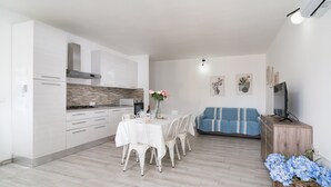 A modern kitchen with white cabinets, a dining table with chairs, a sofa, and a TV on a wooden cabinet. - Apartment 'Celeste' with Private Terrace, Wi-Fi and Air Conditioning (Orosei)