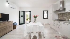 A modern kitchen with white cabinetry, a dining table with chairs, a TV on a wooden cabinet, and a view through an open door. - Apartment 'Celeste' with Private Terrace, Wi-Fi and Air Conditioning (Orosei)