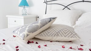 A neatly made bed with patterned pillows, a white bedside table with a lamp, and a white wall. - Apartment 'Celeste' with Private Terrace, Wi-Fi and Air Conditioning (Orosei)