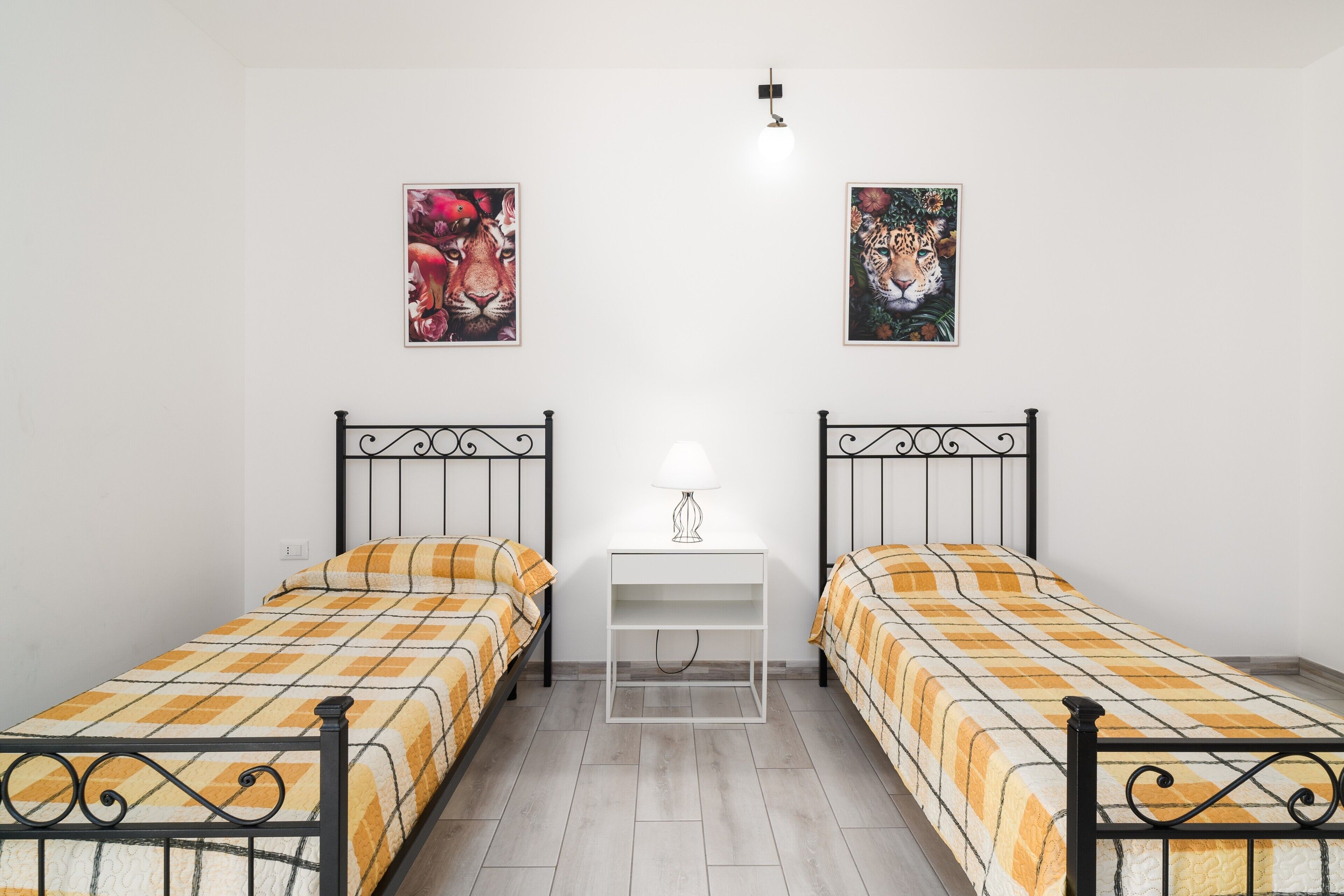 Une chambre avec deux lits, une table de chevet avec une lampe et deux tableaux encadrés au mur.
