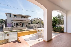 A residential building with a patio area featuring a table and chairs, a gate, and a view of neighboring houses.