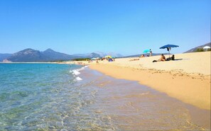 A beach with clear water, people sunbathing, and umbrellas.