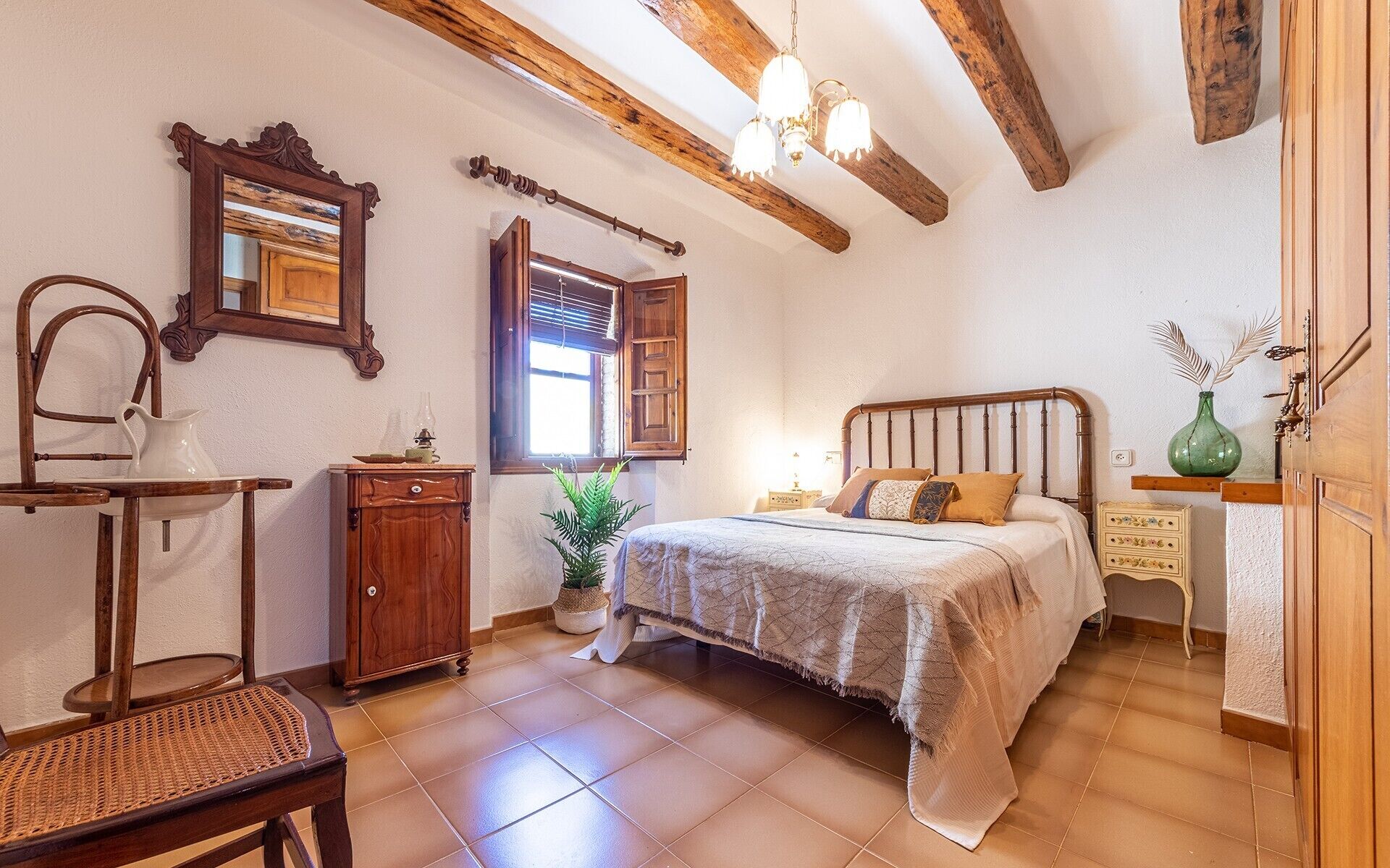 Un dormitorio con cama, muebles de madera, una ventana con contraventanas y una araña.