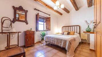 Un dormitorio con cama, muebles de madera, una ventana con contraventanas y una araña.