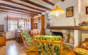 Uma sala de estar aconchegante com vigas de madeira, lareira e um espaço de jantar com mesa e cadeiras.