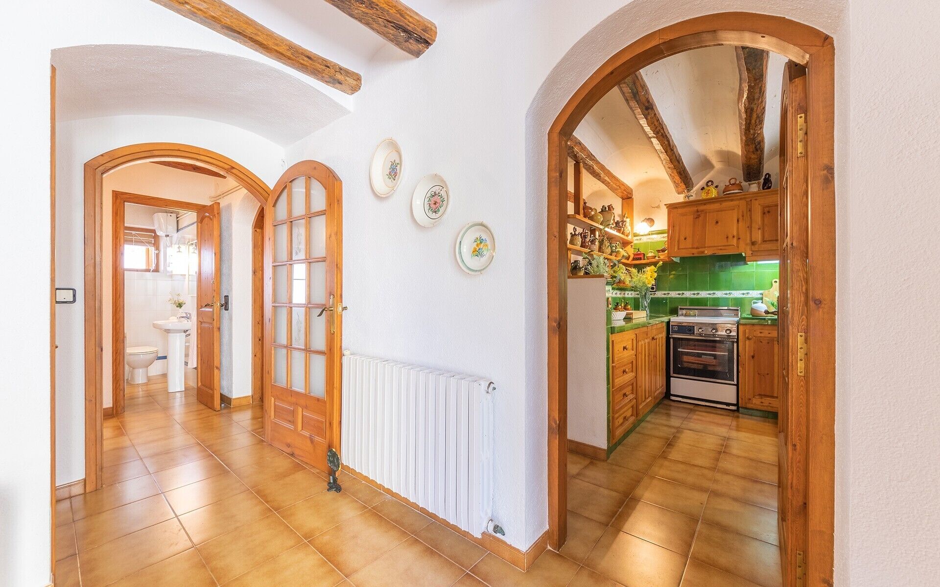 Un pasillo con puertas de madera, un radiador y una cocina con armarios de madera y una estufa.