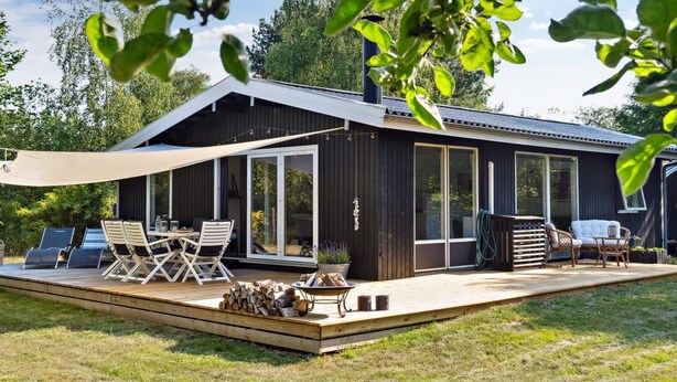 Et moderne hus med terrasse, udendørs møbler og et stort vindue.
