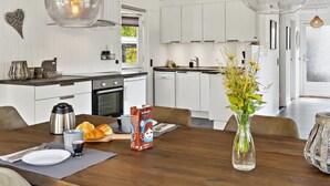 Et moderne køkken med hvide skabe, et spisebord dækket med en vase blomster, og en kaffemaskine.