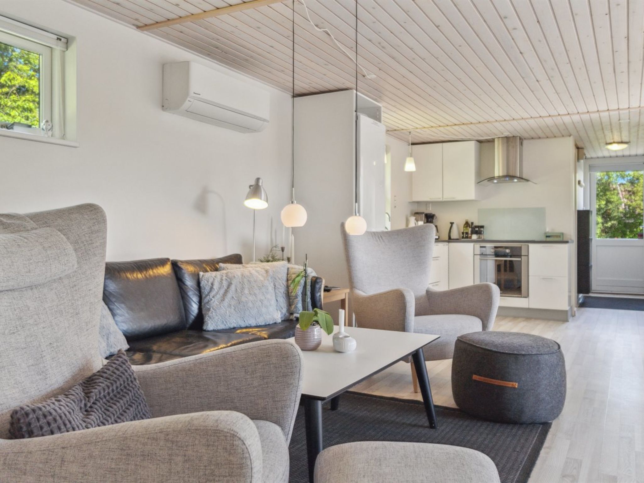 A modern living room with a sofa, chairs, a table, and a kitchen in the background.