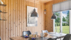 Ein Zimmer mit Holzvertäfelung, einem Esstisch, Stühlen, einer Pendelleuchte und einem Fenster mit Blick ins Grüne.