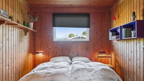 Ein gemütliches Zimmer mit Holzwänden, einem Bett mit weißer Bettwäsche, einem Fenster mit Ausblick und Regalen mit Büchern und Dekoration.