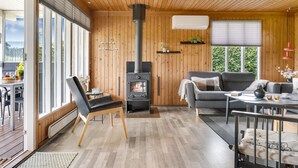 Ein gemütliches Blockhaus-Interieur mit Kaminofen, einer Couch, einer Essecke und großen Fenstern.