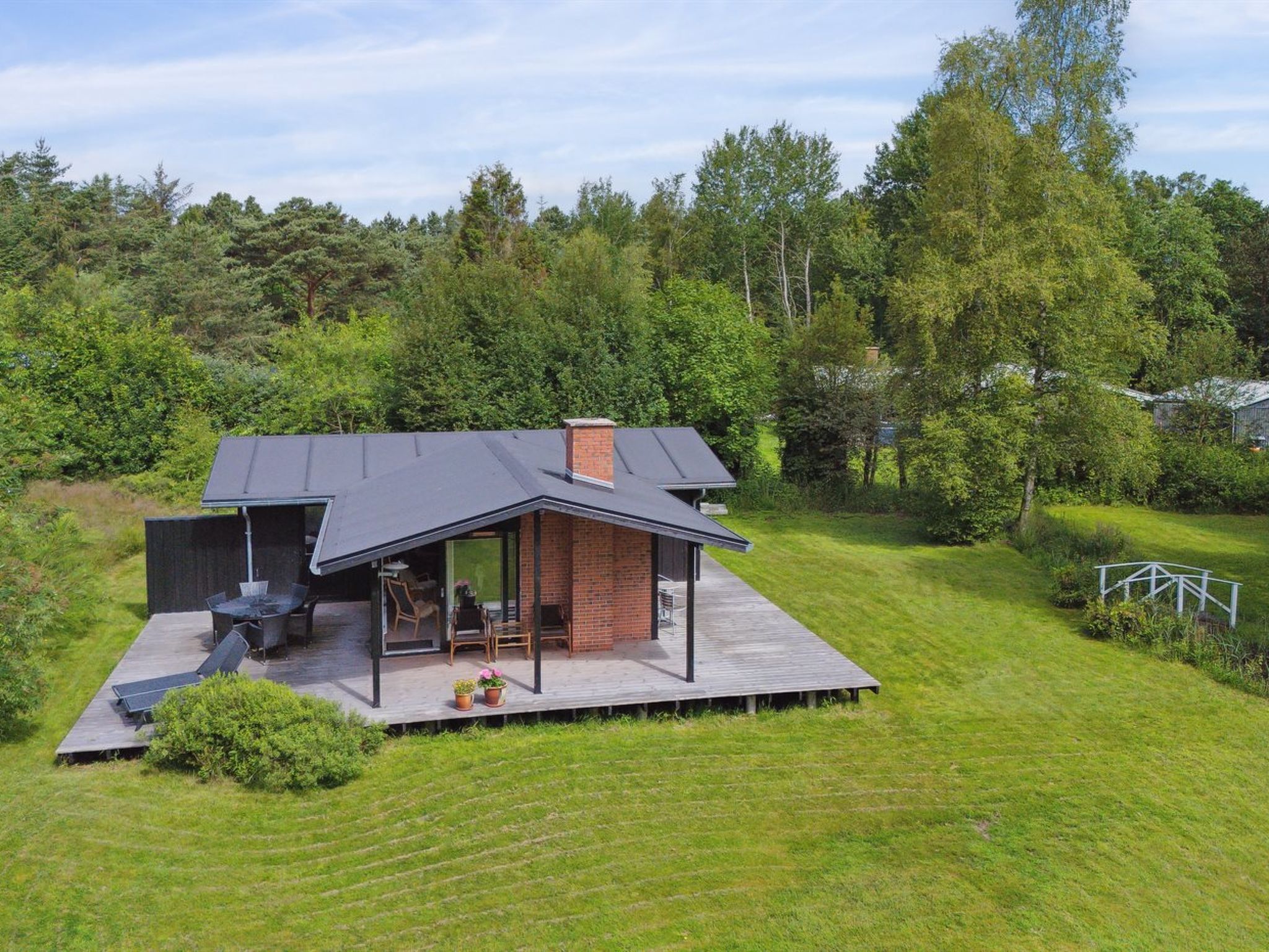 Une maison moderne dotée d’un patio couvert, d’une cheminée en briques et d’une terrasse.