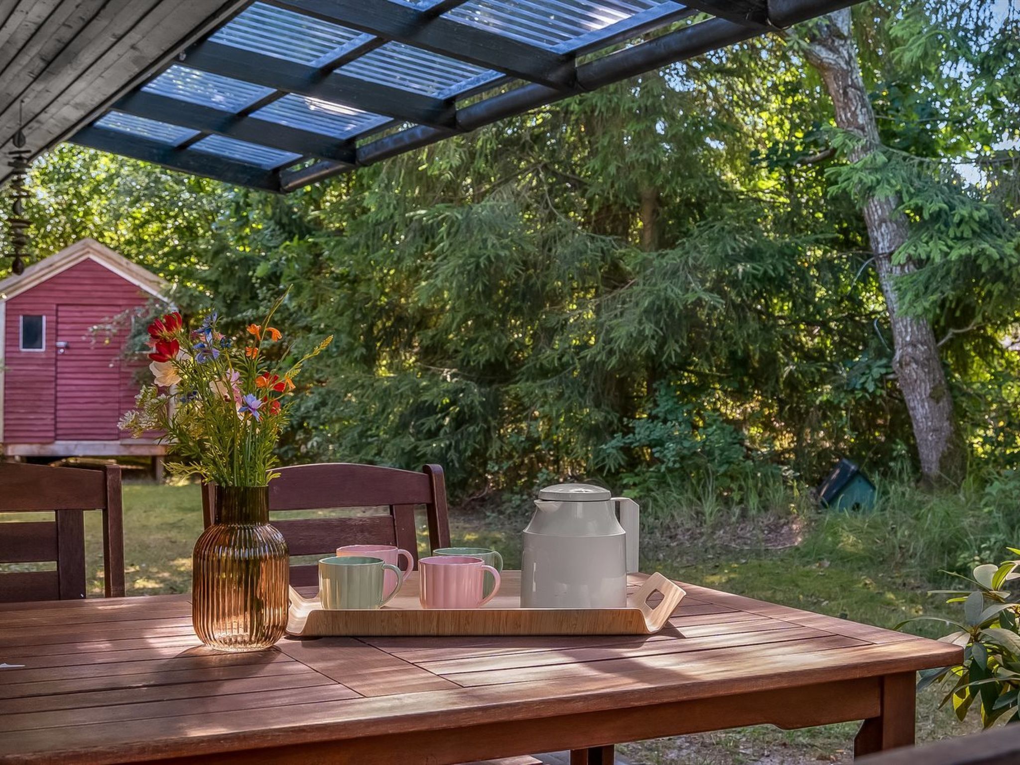 A wooden table with a tray holding a pitcher, cups, and a vase with flowers.