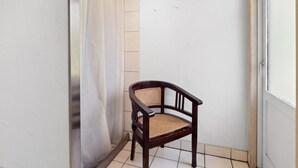 Un pequeño balcón cerrado con una silla de madera y una cortina blanca.