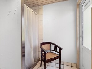 Un pequeño balcón cerrado con una silla de madera y una cortina blanca.