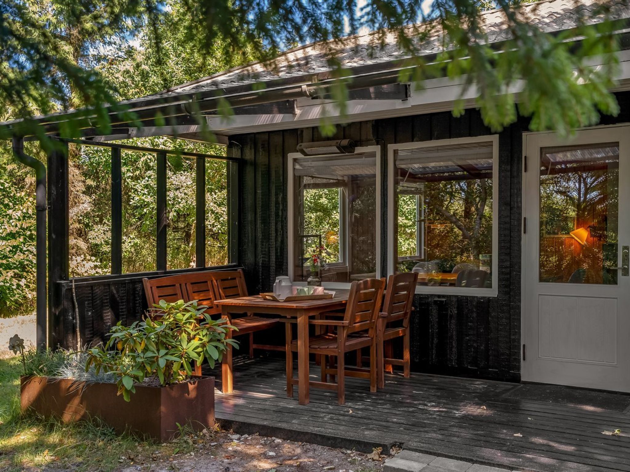 Eine Holzterrasse mit Tisch und Stühlen, umgeben von viel Grün.