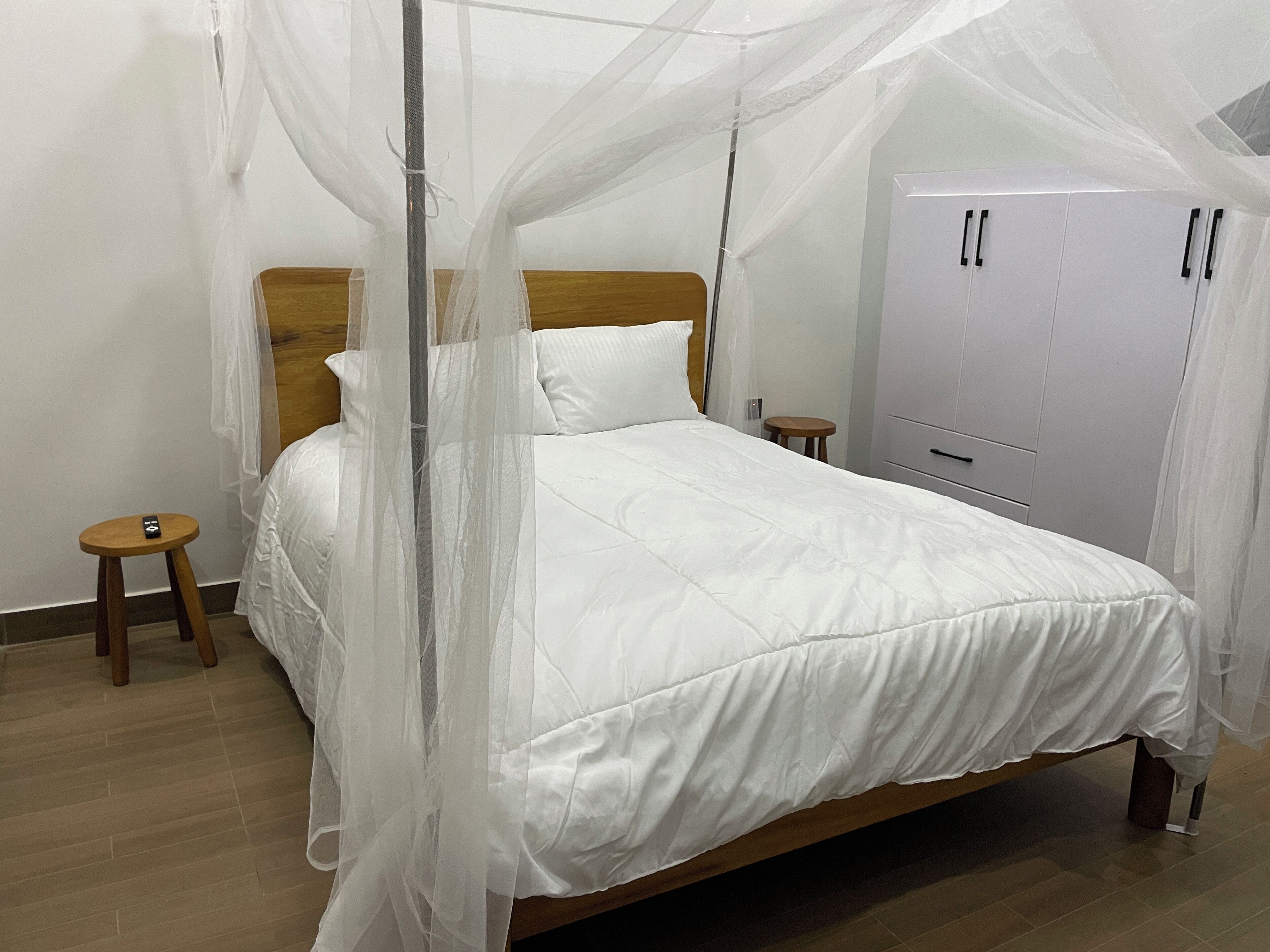 A neatly made bed with a canopy, a wooden headboard, a bedside table, and a wardrobe.