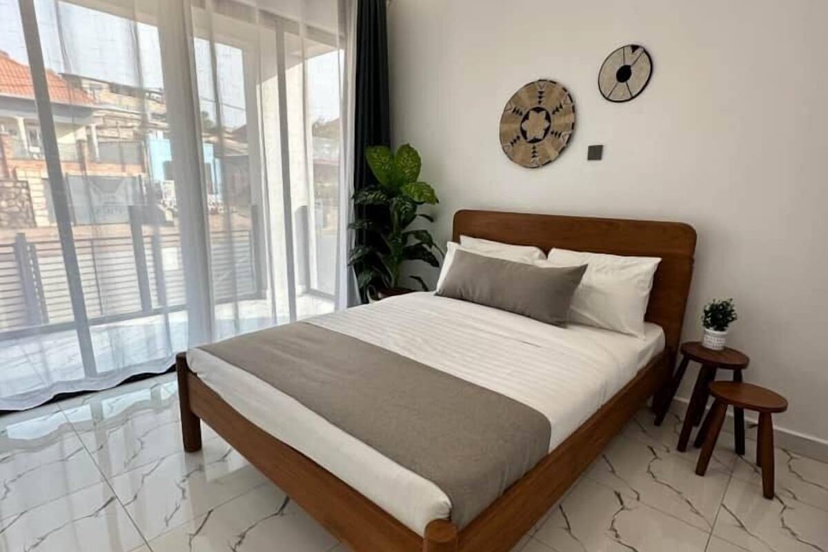 A bedroom with a bed, a potted plant, and a view of the outside.