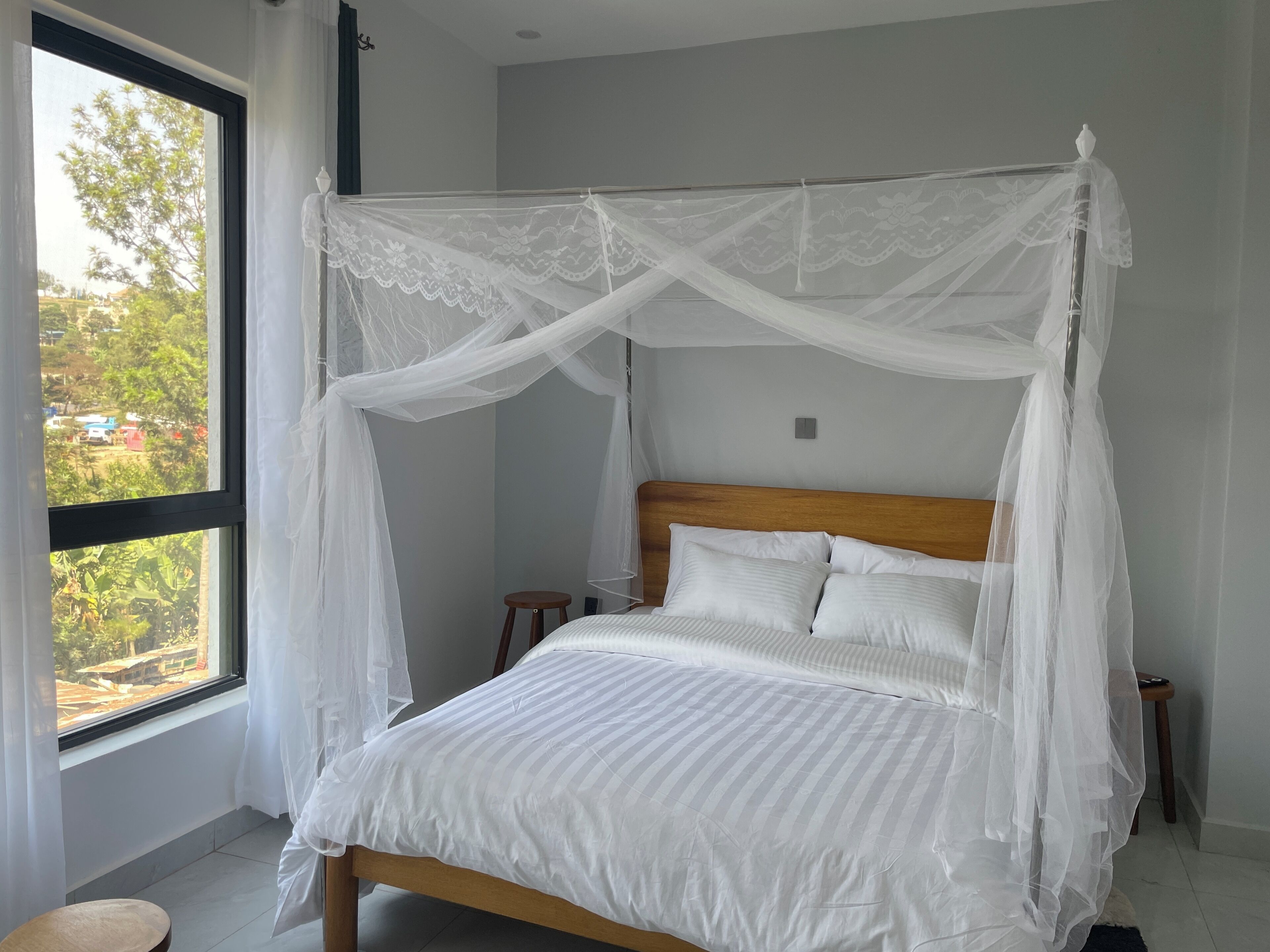 A bed with a canopy, a window, and a view of greenery outside.