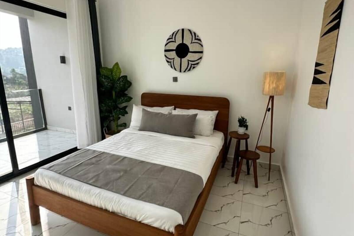 A modern bedroom with a large bed, a floor lamp, and a view through a sliding door.
