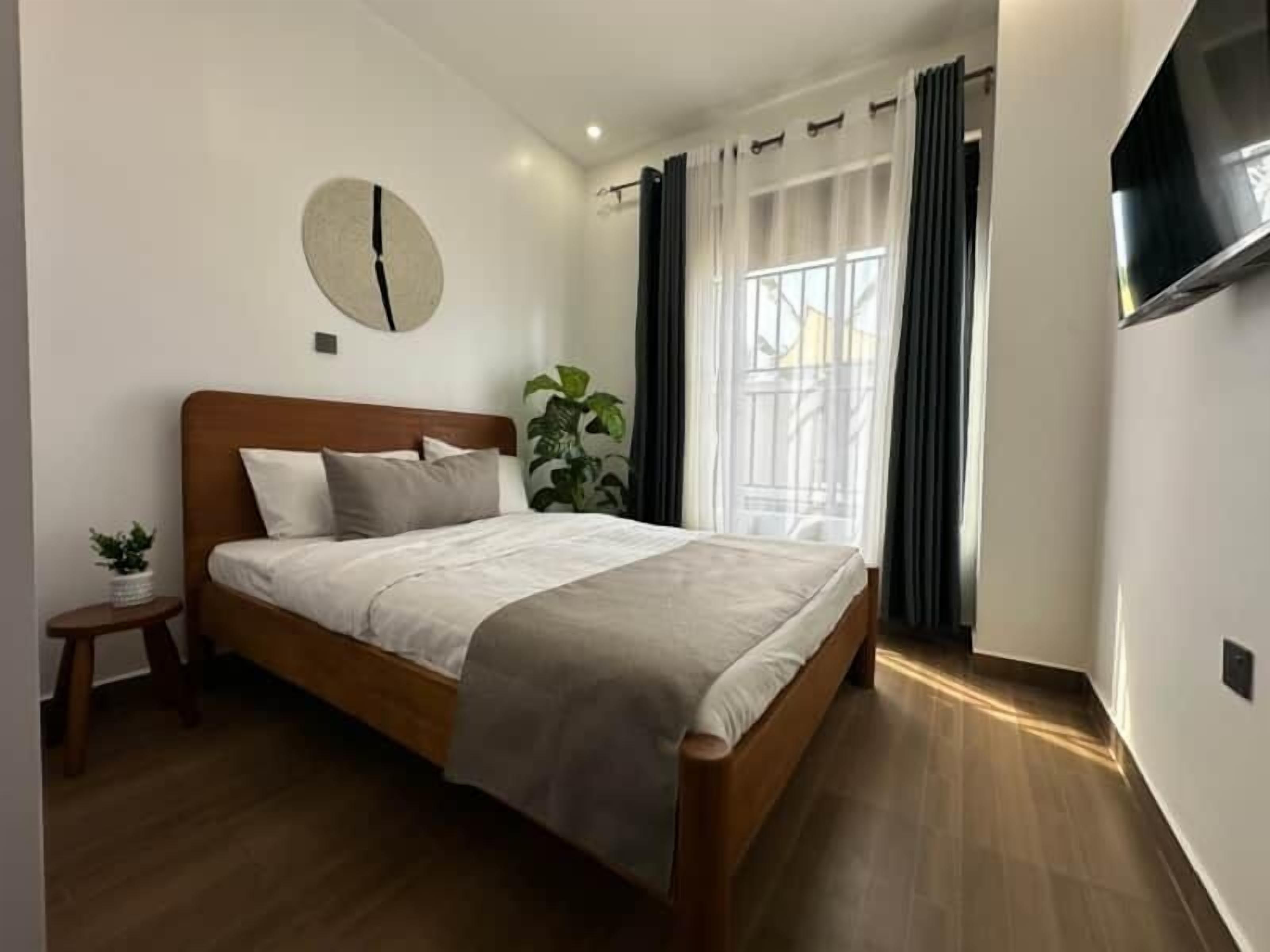 Un dormitorio con una cama de madera, un reloj de pared redondo, una planta en maceta y un televisor fijado a la pared.