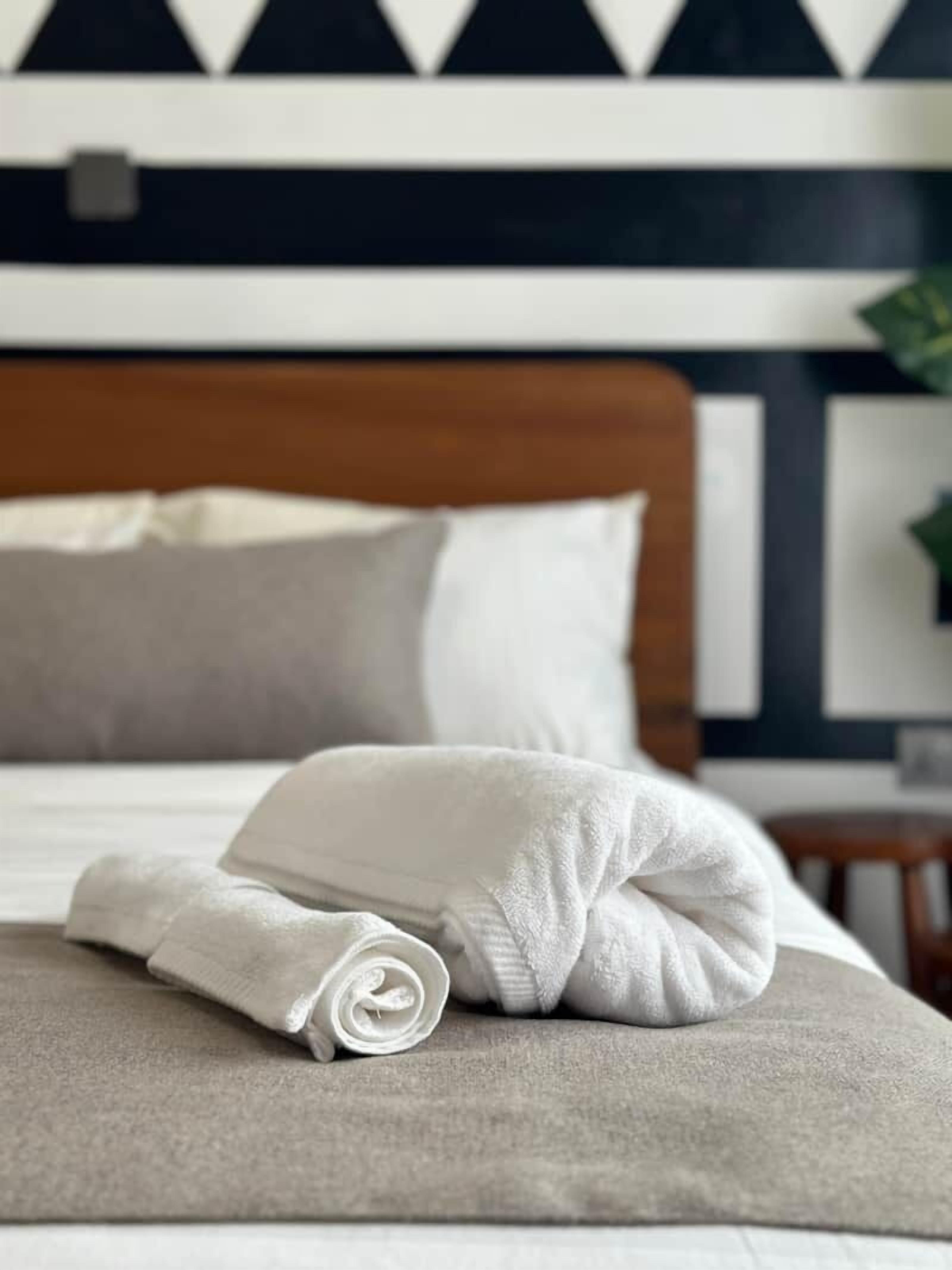 A neatly made bed with a rolled white towel and a folded white pillow.