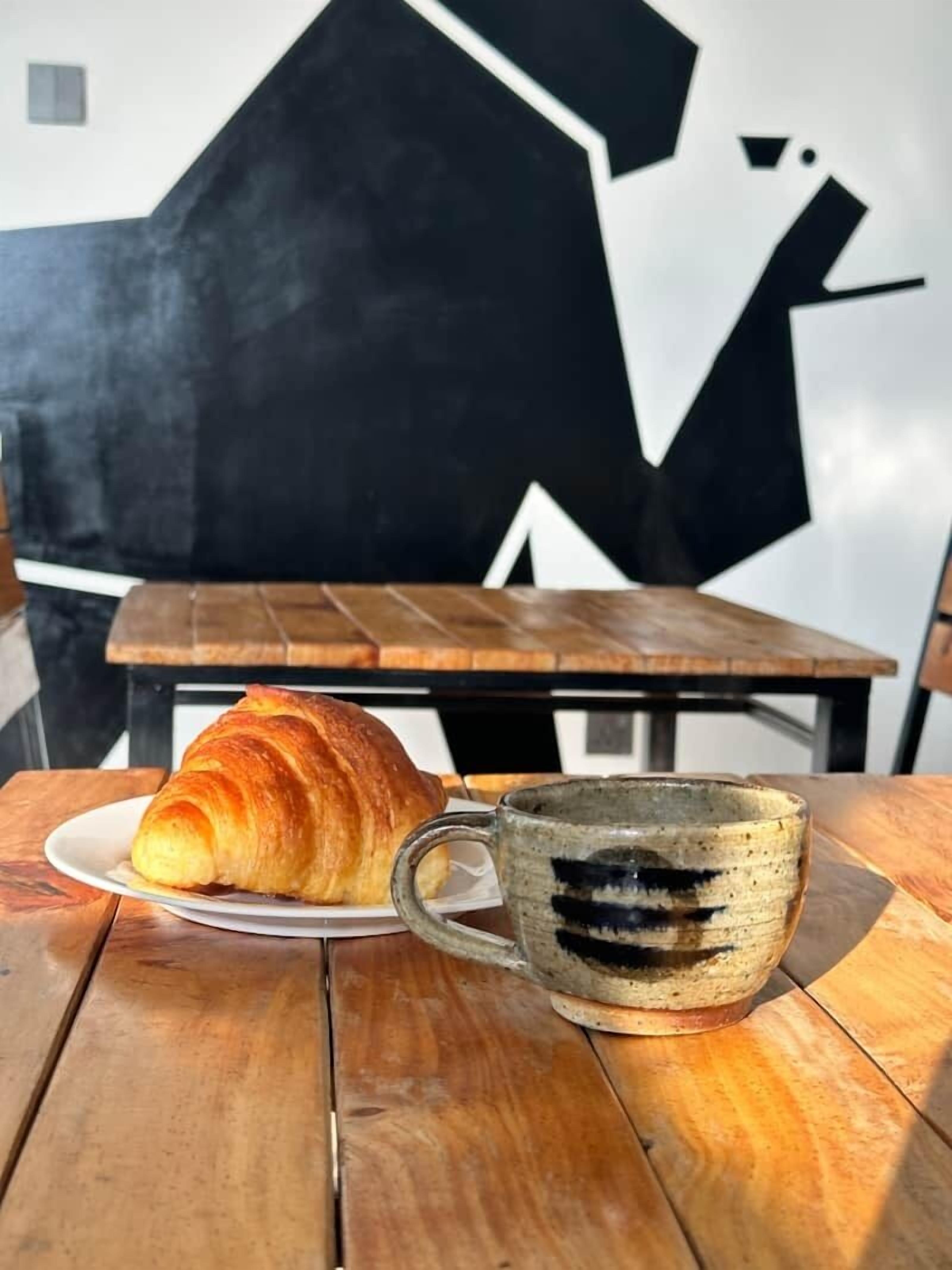 A wooden table with a croissant and a mug.